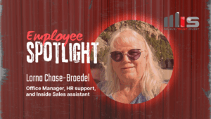 A circular portrait photo of Lorna Chase-Broedel smiling outdoors with rocky landscape and trees in the background, set against a red corrugated metal backdrop with a dramatic spotlight effect. Text identifies her as Office Manager, HR Support, and Inside Sales Assistant."